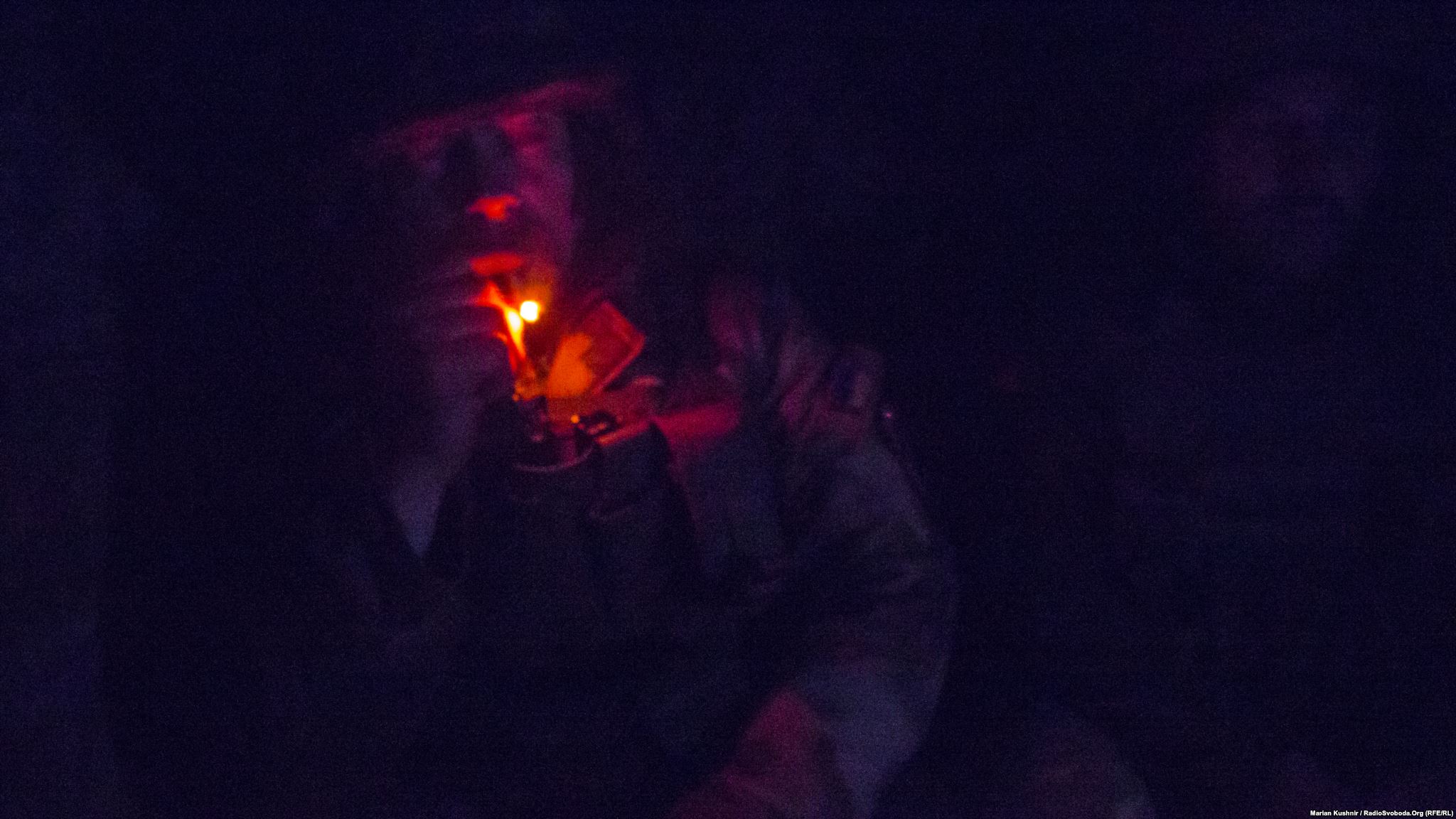 In total darkness of a dugout, Mykhajlo smokes while on watch in frontline positions