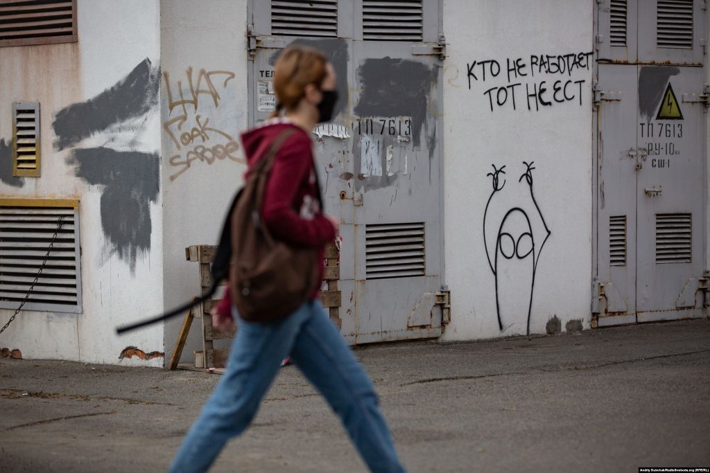 Дівчина проходить повз трансформаторну будку з графіті «Хто не працює, той не їсть». Фото - Андрій Дубчак